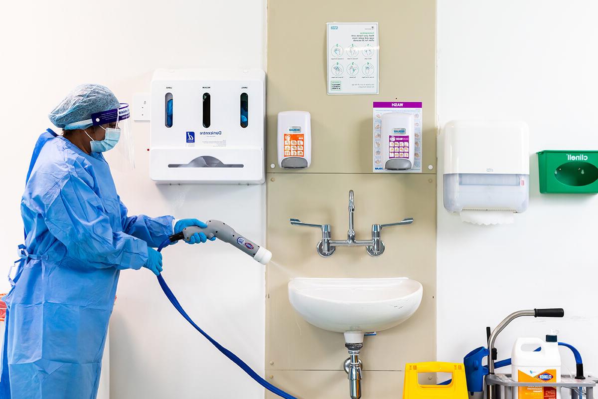 一名穿着蓝色个人防护装备的妇女正在使用专业软管在临床环境中喷洒白色水槽